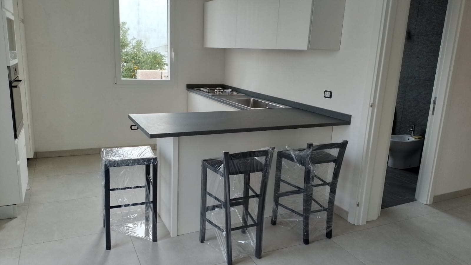 Una piccola cucina bianca con un piano di lavoro scuro e tre sgabelli neri.