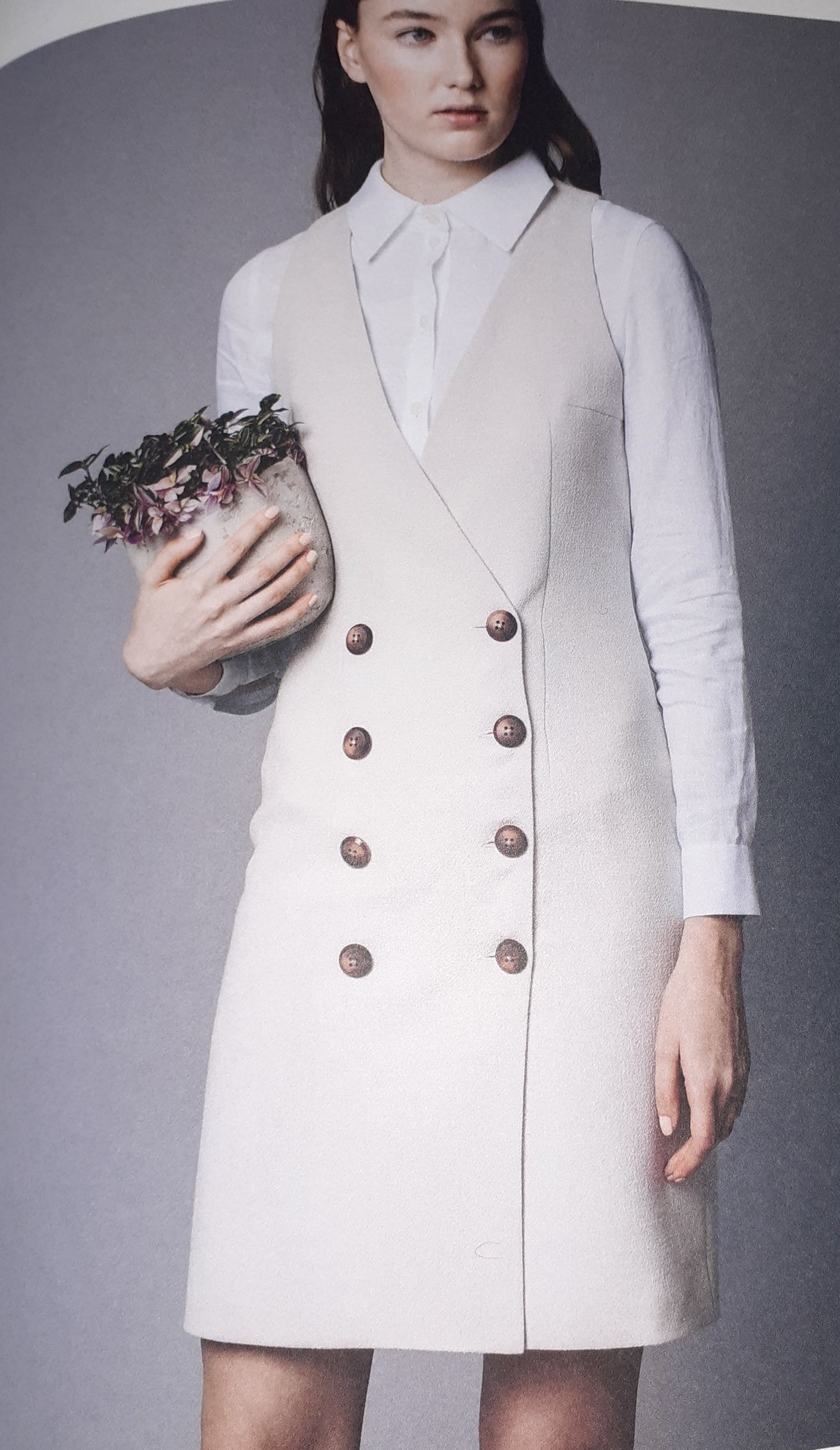 Vrouw in een witte lange jas houdt een potplant vast.