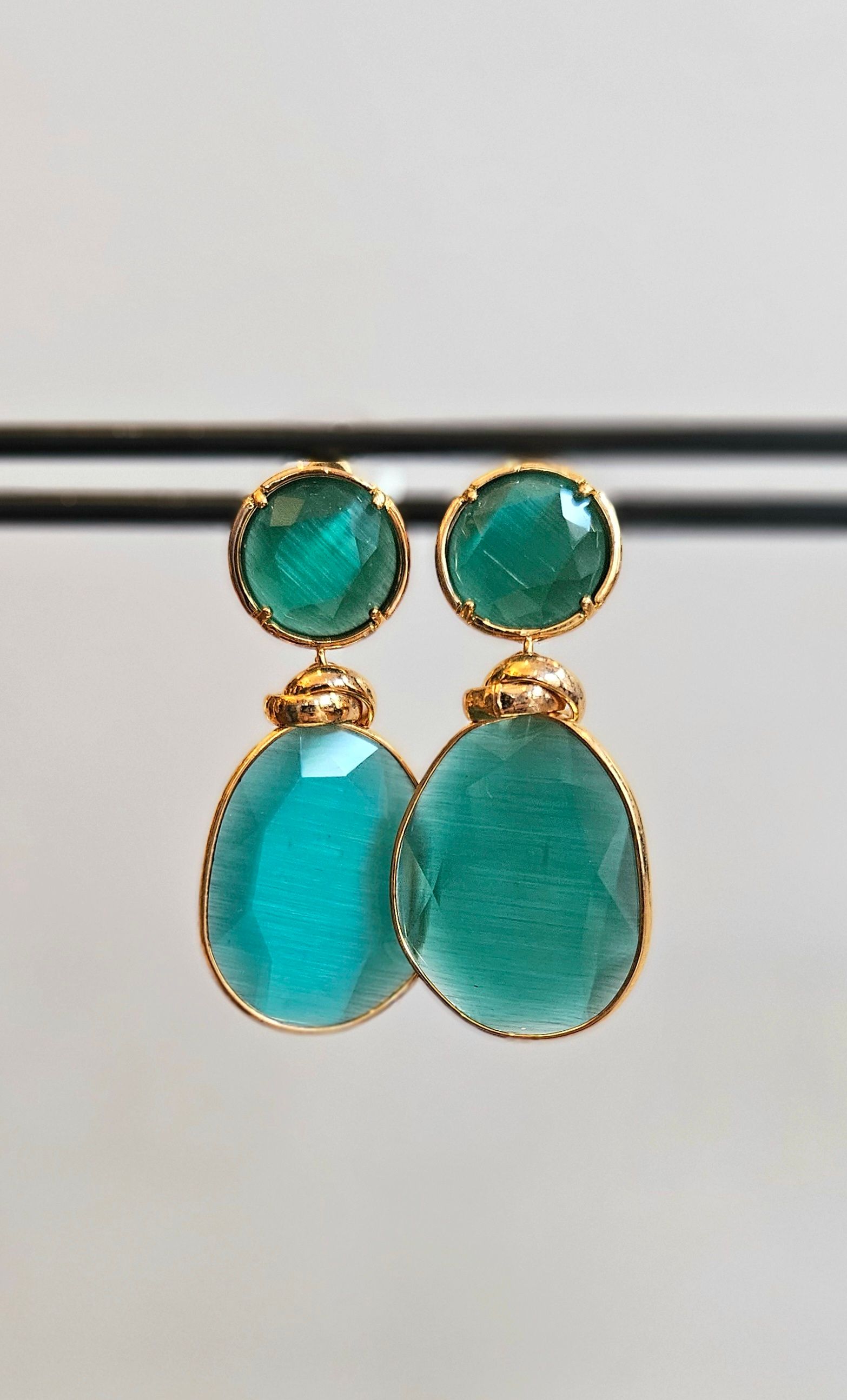 Een paar groene oorbellen liggen tegen een grijze achtergrond