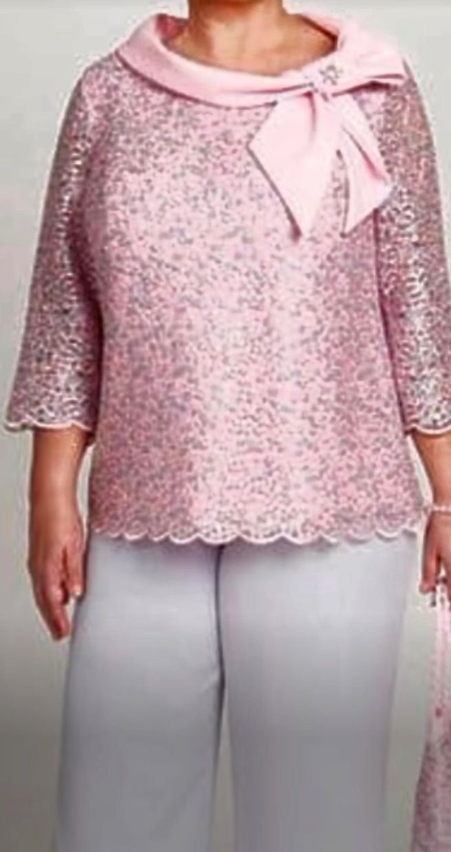 Een vrouw met een maatje meer draagt ​​een roze kanten topje en een witte broek.