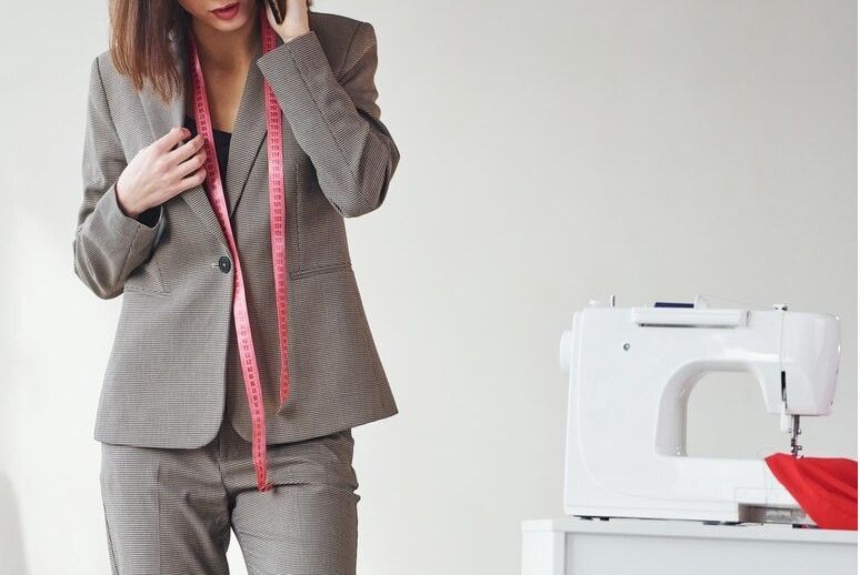 Een vrouw in een mooi grijs pak staat naast naaimachine.
