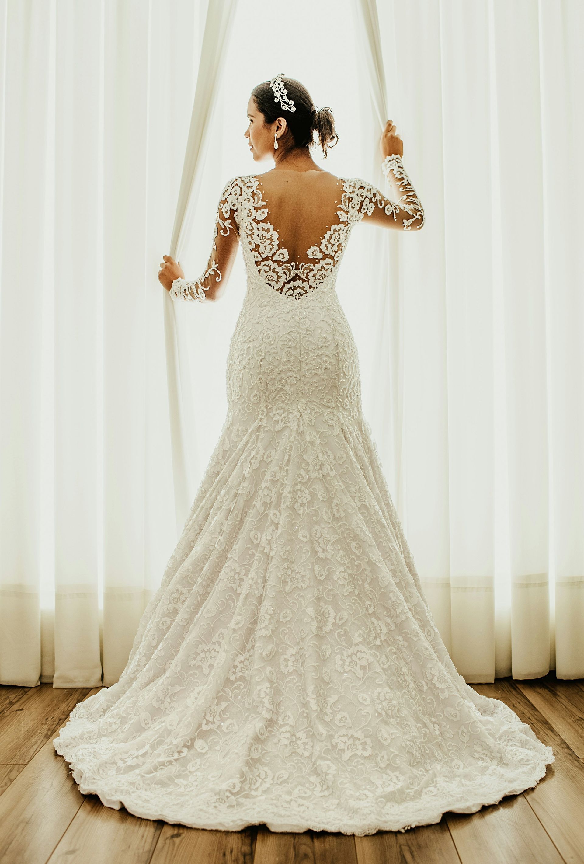 vrouw in een trouwjurk staat voor een raam.