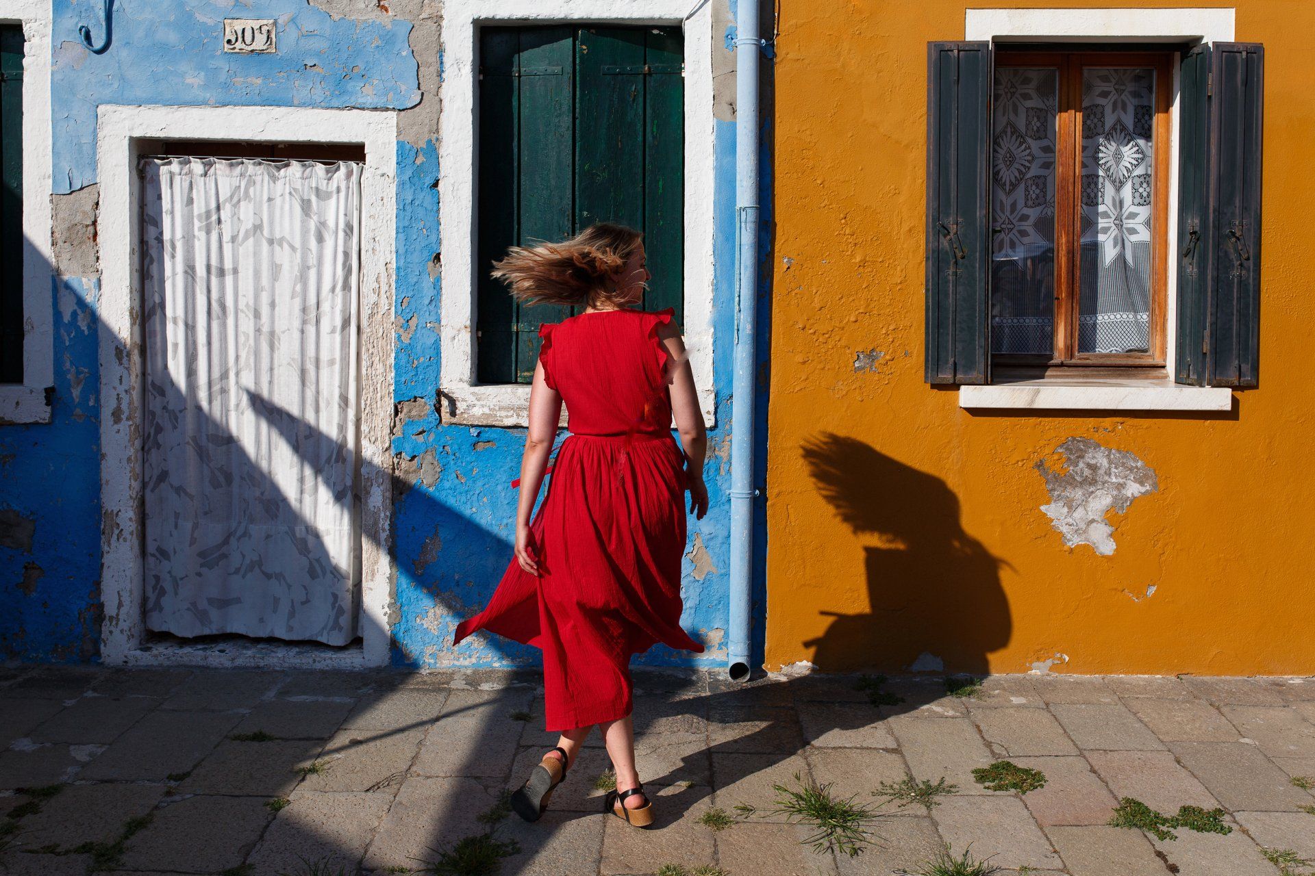 Girl in red dress twirls in front of rustic and colourful fishermen's houses on the Venetian island of Burano.