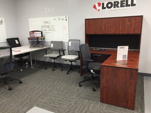 A room with a desk , chairs , and a whiteboard.