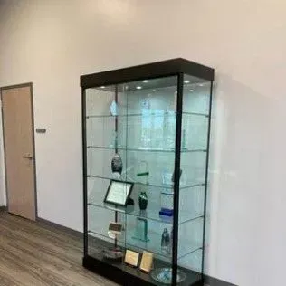 A glass display case filled with trophies and plaques in a room.