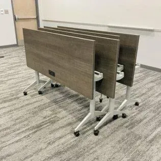 A row of folding tables are stacked on top of each other in a room.