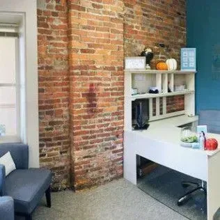 A room with a brick wall , a desk , a chair and a window.