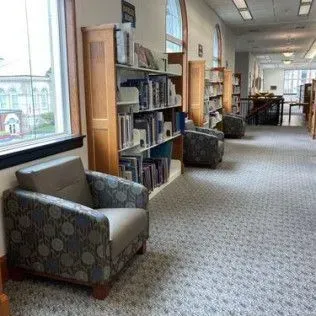 A long hallway in a library with chairs and bookshelves.