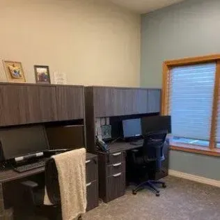 A room with two desks , a chair , a computer and a window.