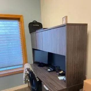 There is a desk with a computer on it in a room with a window.