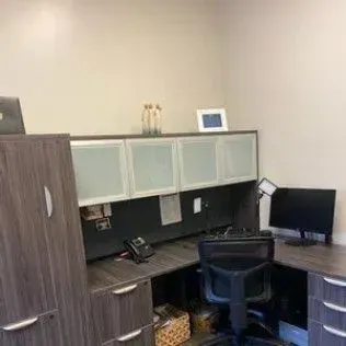 A cubicle with a desk , chair , computer and cabinets.