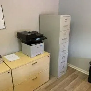 A printer is sitting on top of a wooden dresser next to a filing cabinet.