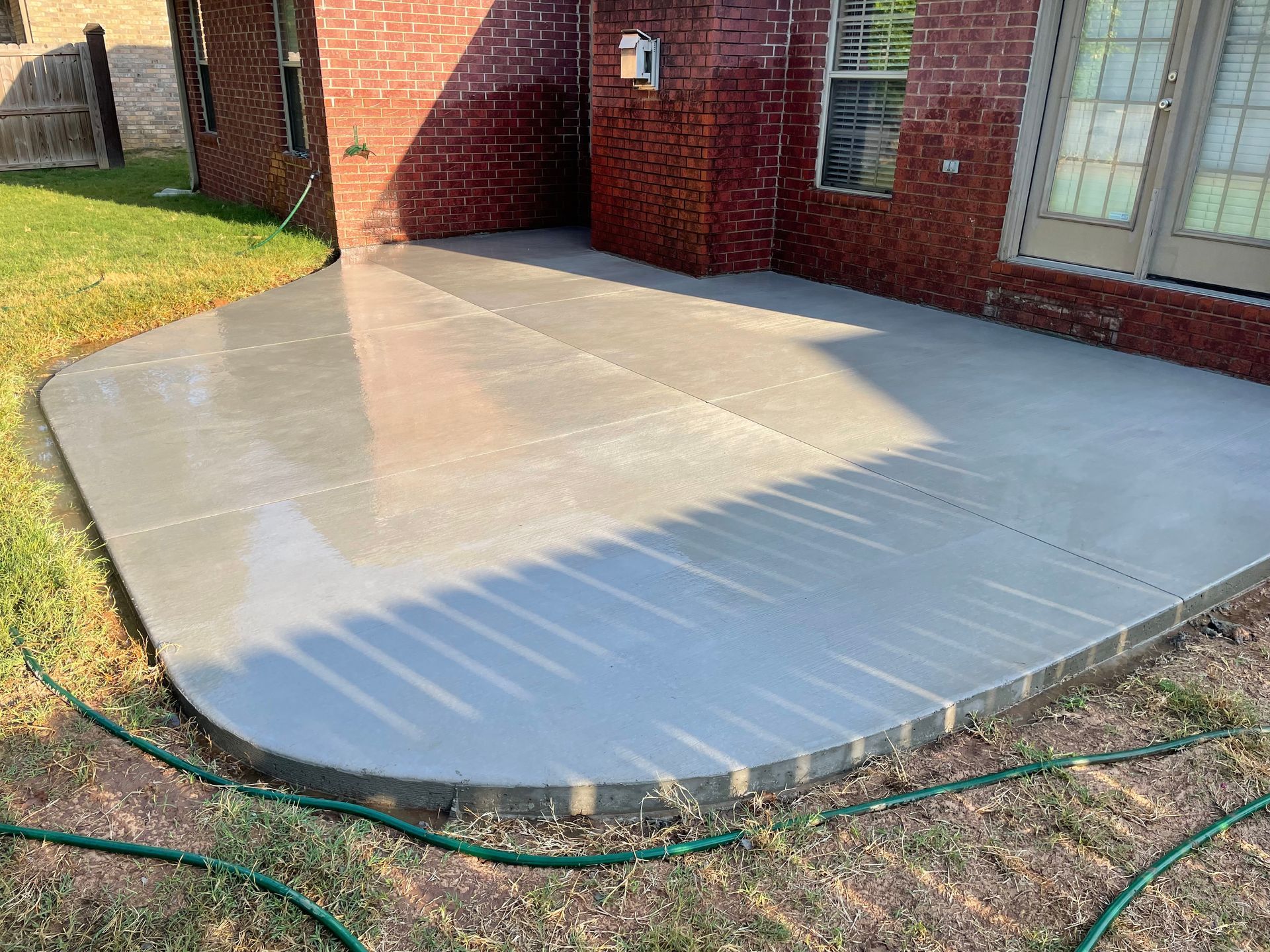 A concrete patio in front of a brick house with a hose.