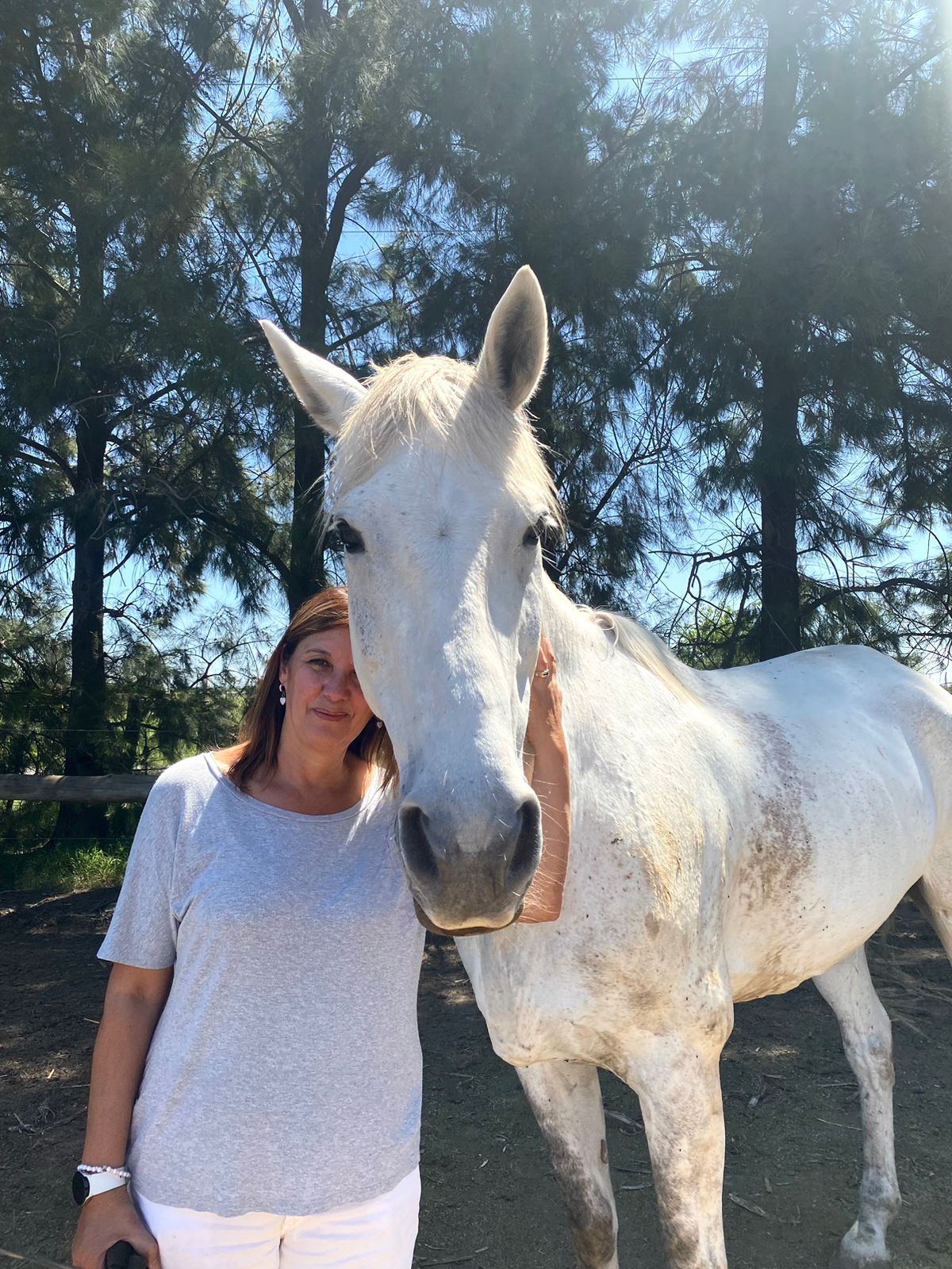 Una mujer está parada junto a un caballo blanco.