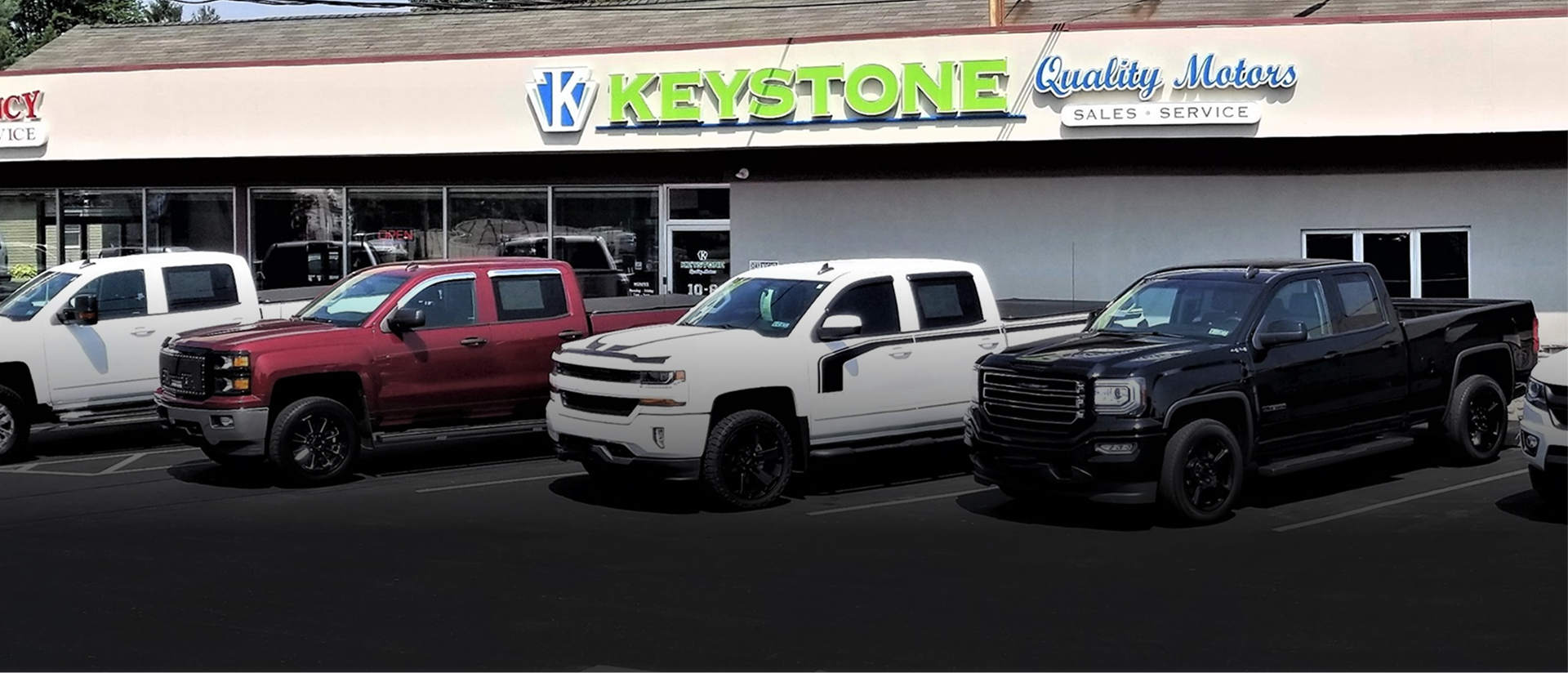 Car dealership lot with several pickup trucks parked in front of a Keystone building | Keystone Quality Motors