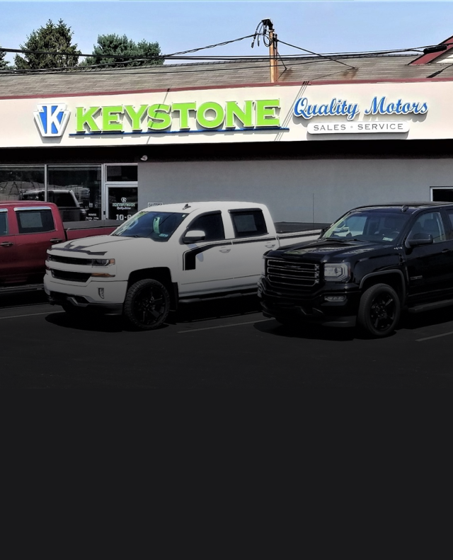 Two parked pickup trucks in front of Keystone Quality Motors dealership sign | Keystone Quality Motors