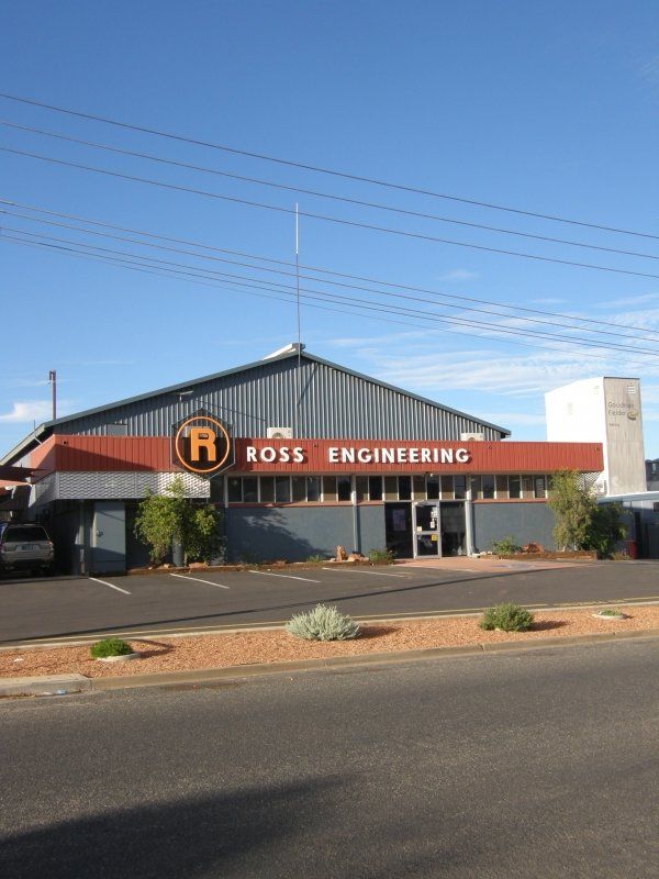 Ross Engineering building with gray exterior, orange and black signage, and clear blue sky.