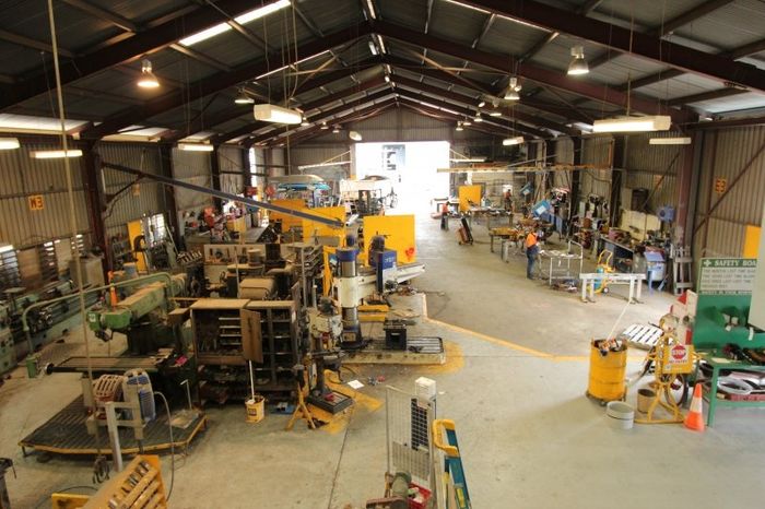 Wide shot of a bustling metal workshop.  Machinery, tools, and workers are spread throughout the large, open space.