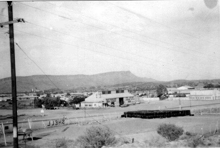 Black and white photo of an older townscape. A sign for Shell and a mountain are in the distance.
