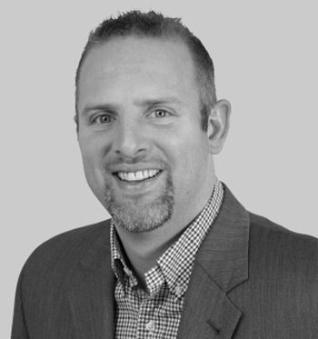 A man in a suit and plaid shirt is smiling in a black and white photo.