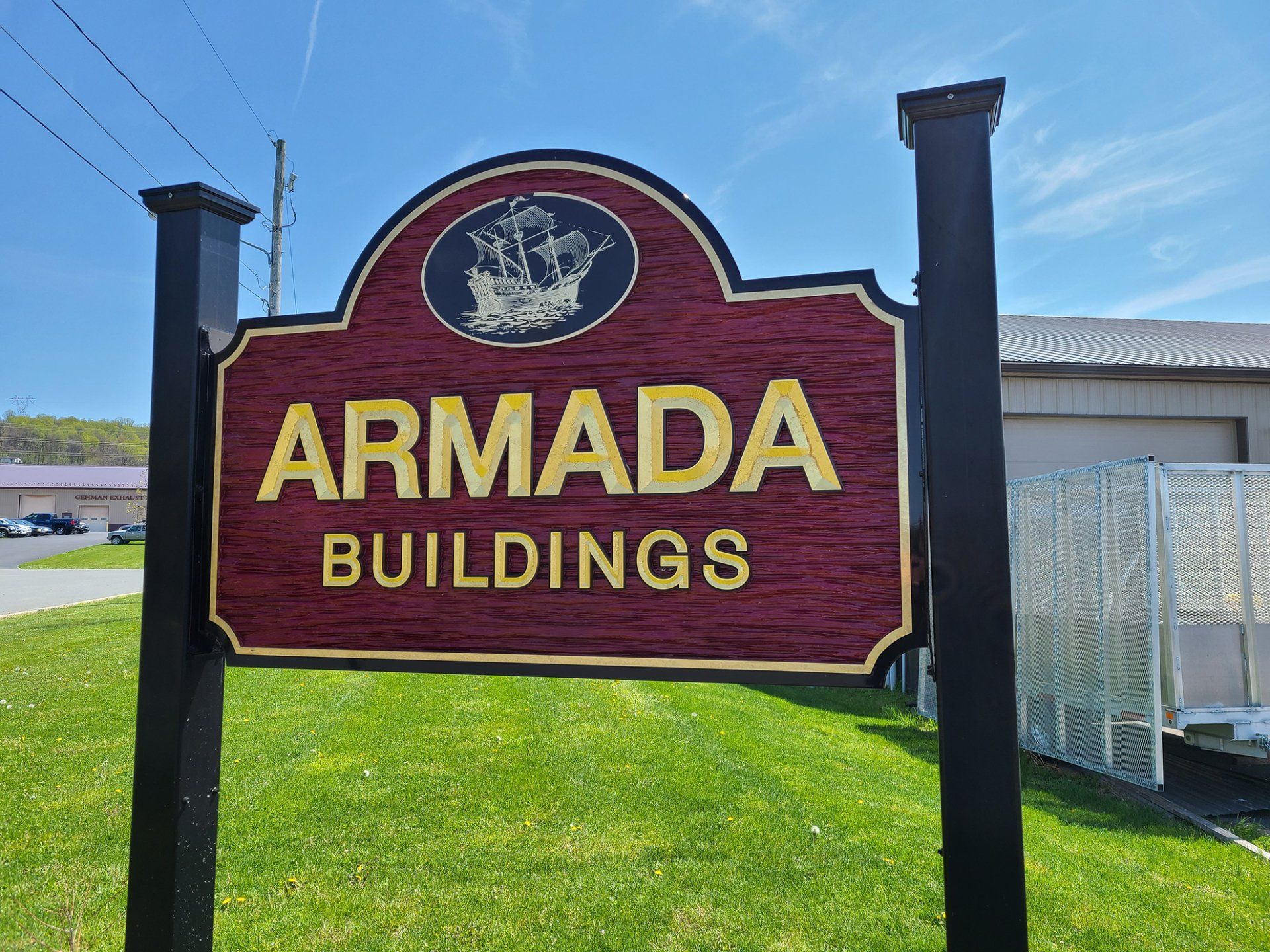A wooden sign for armada buildings is sitting on top of a lush green field.