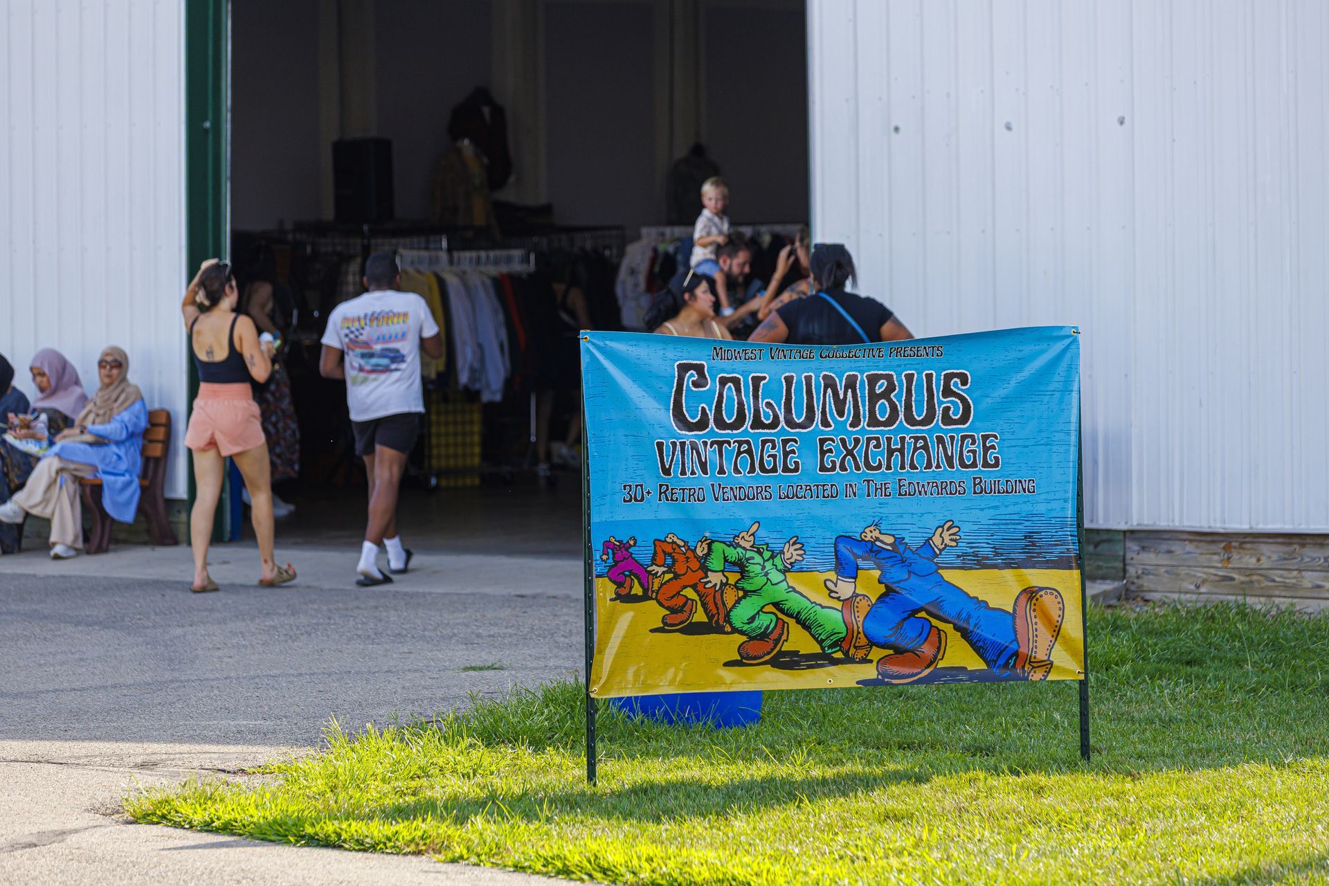 Sign for Columbus Vintage Exchange, banner shows cartoon figures, people in front of open doorway, some seated.