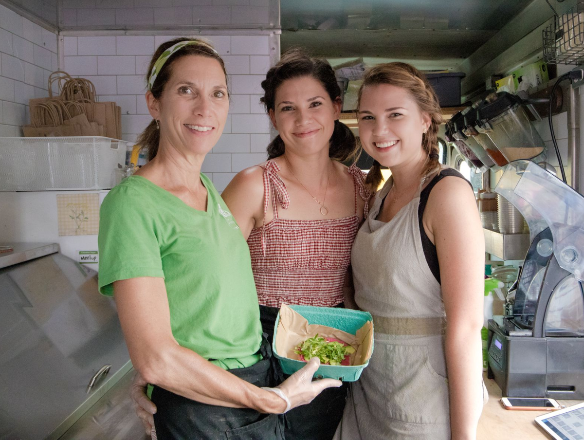 Three people in a kitchen holding a bowl of food, smiling at the camera.