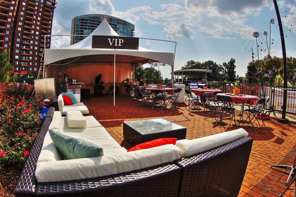 Outdoor VIP seating area with white canopy, tables, and lounge seating; sunny day.
