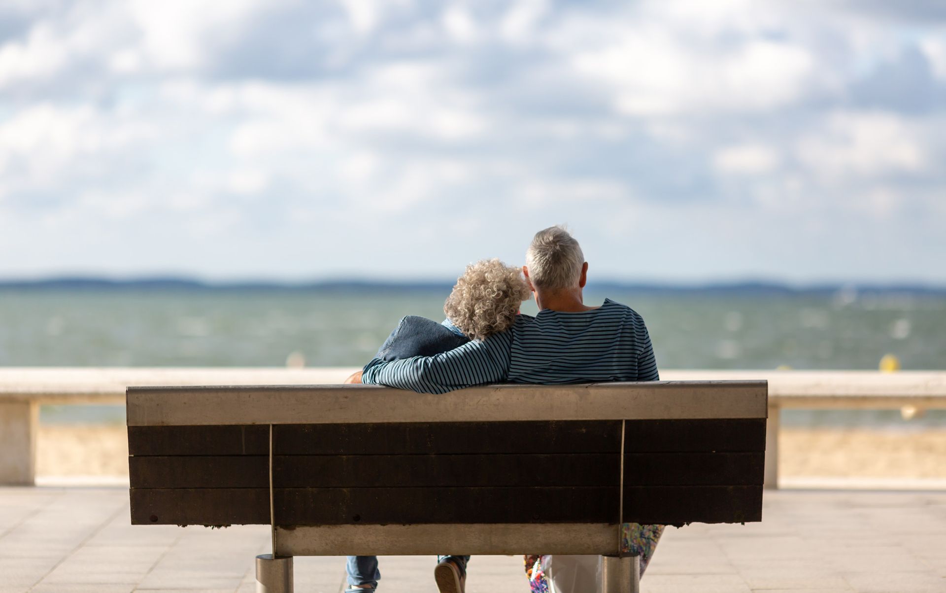 A man and a woman are sitting on a bench looking at the ocean.