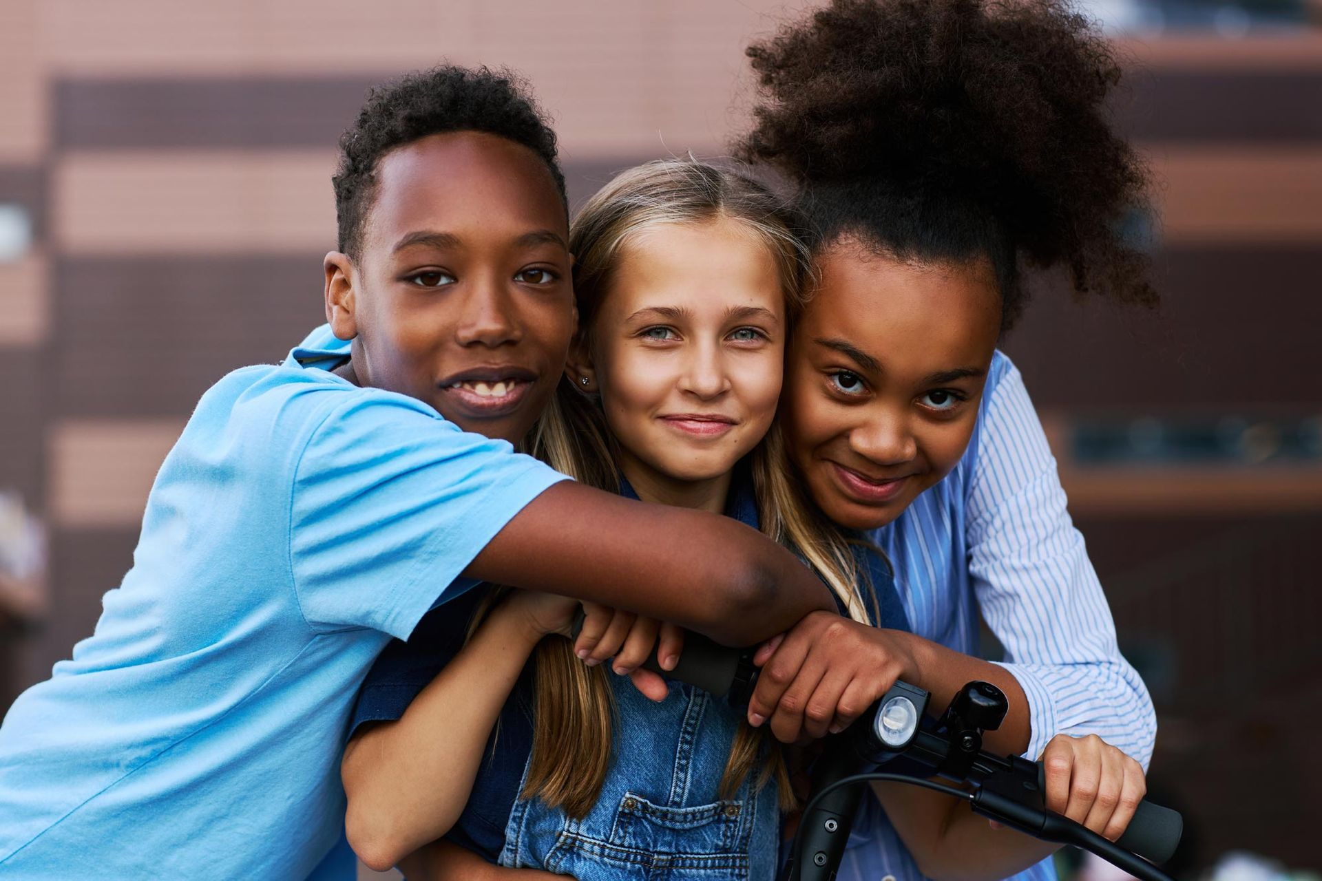 A boy and two girls are hugging each other in front of a building.