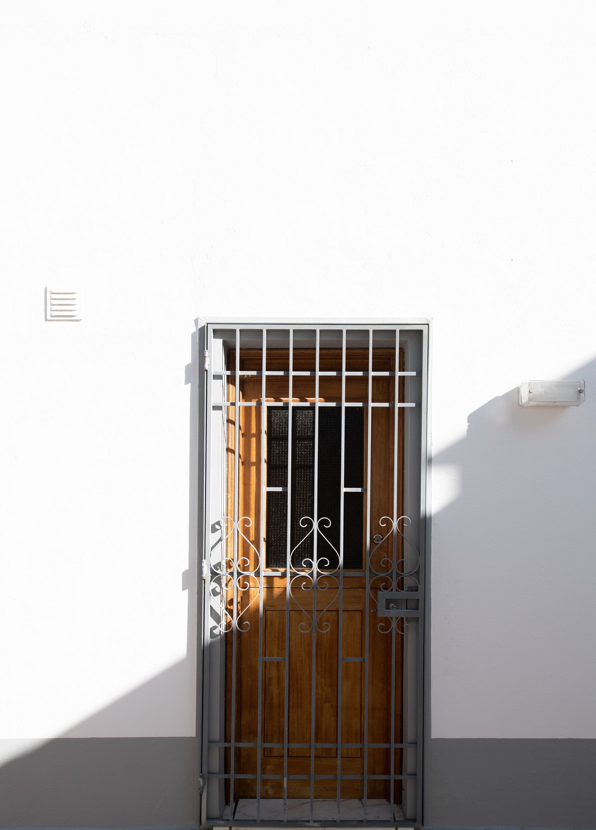 Una porta di legno con un cancello di metallo su un muro bianco.