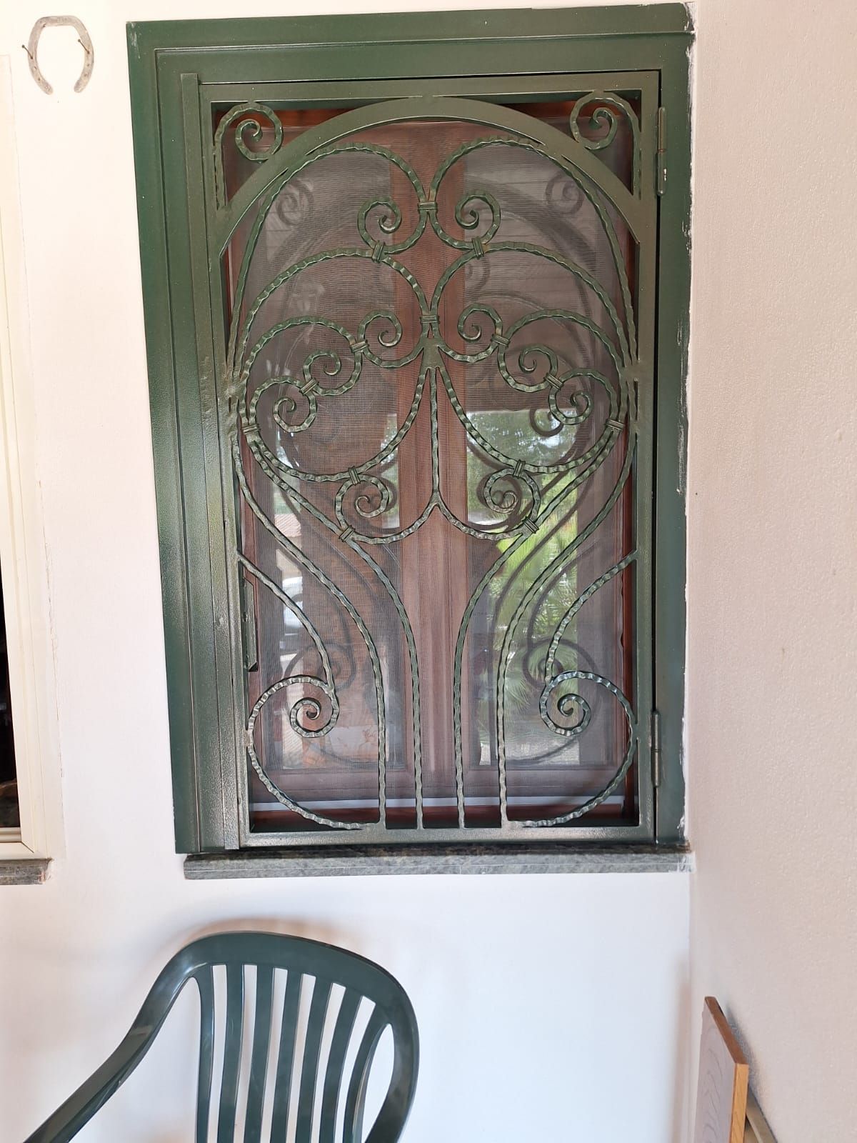 Una sedia verde è appoggiata davanti a una finestra con una grata in ferro battuto.