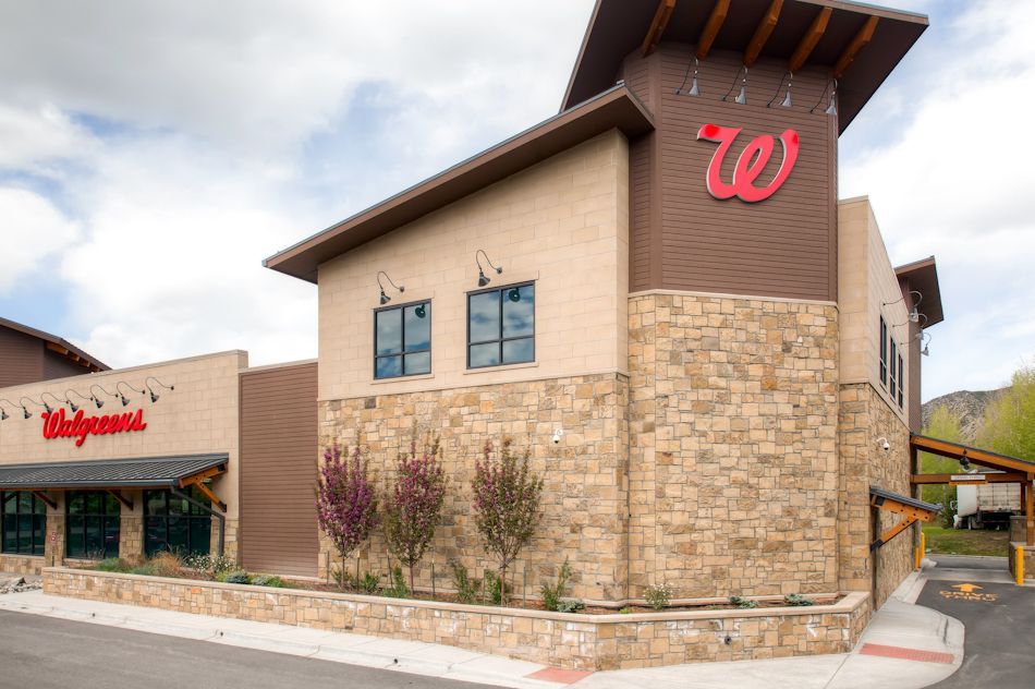 A modern stone and tan stucco Walgreens pharmacy building under a cloudy sky.