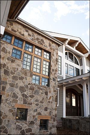 A stone-walled building exterior with multi-pane wooden windows and a covered entrance in a mountain-style home design.