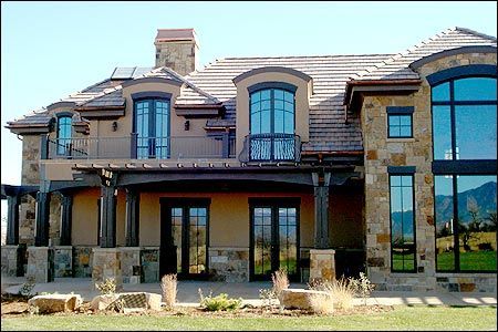 A multi-story stone and stucco home with dark window frames, a tiled roof, and a covered patio area.