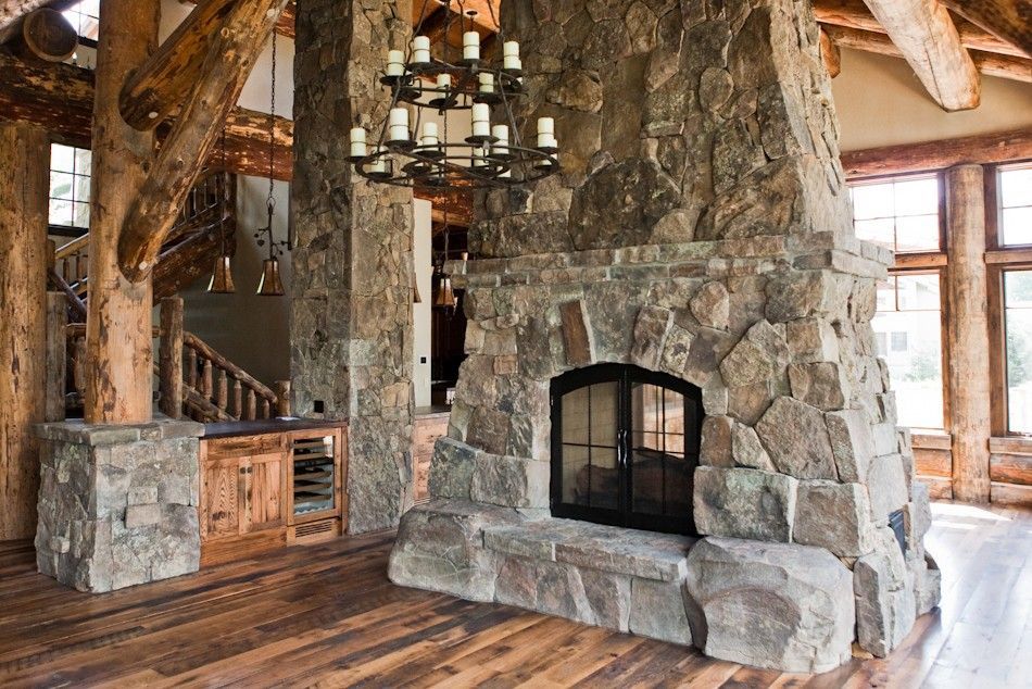 Rustic living room featuring a massive floor-to-ceiling stone fireplace, heavy log pillars, and a wooden wine cooler.