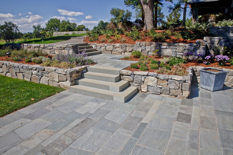 Stone steps lead up a terraced garden featuring fieldstone retaining walls and a blue-gray flagstone patio.