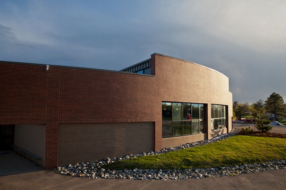 A curved red brick building with large windows, set against a blue, partly cloudy sky with a landscaped rocky garden.