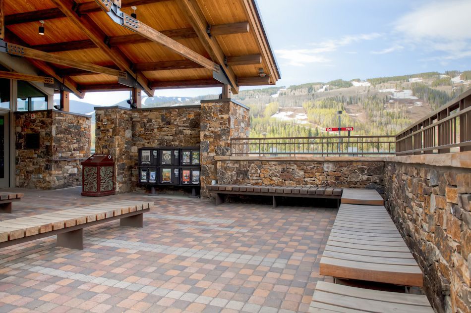 Four dark wicker chairs with red cushions arranged on a stone paver patio in a backyard.