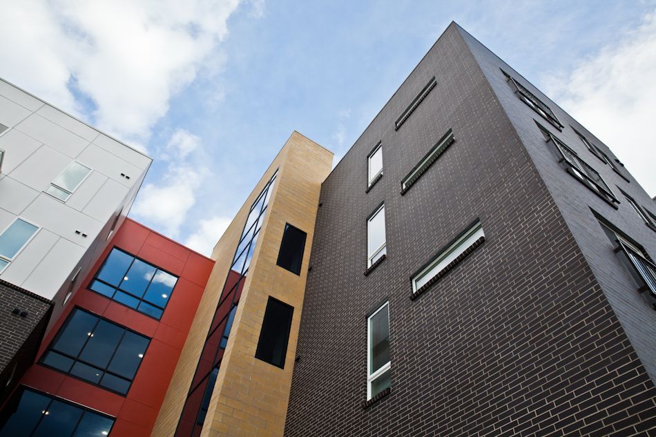 A low-angle view of modern multi-story buildings with white, red, tan, and dark brick facades under a cloudy sky.