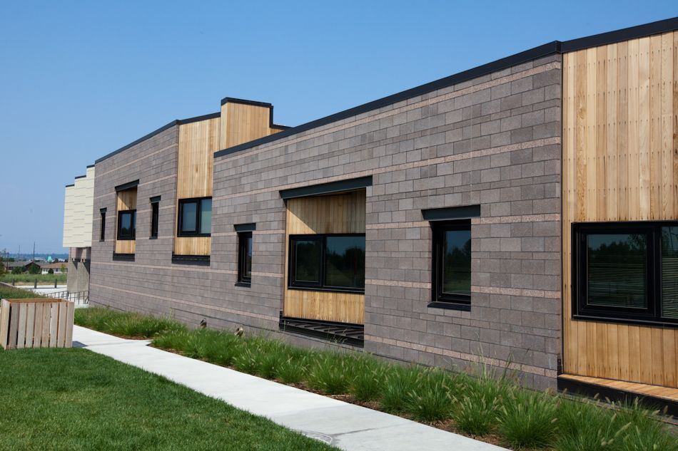 Modern building exterior with gray concrete block walls and vertical wood paneling along a landscaped concrete walkway.