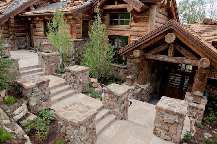 A backyard featuring a stone patio, a small lawn with stepping stones, a wooden privacy fence, and dark mulch beds.