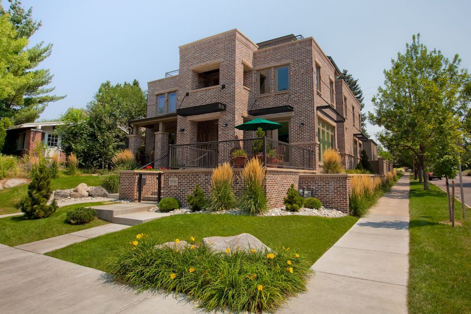 A multi-story brick residential building with a front lawn, sidewalk, and landscaping on a sunny day.