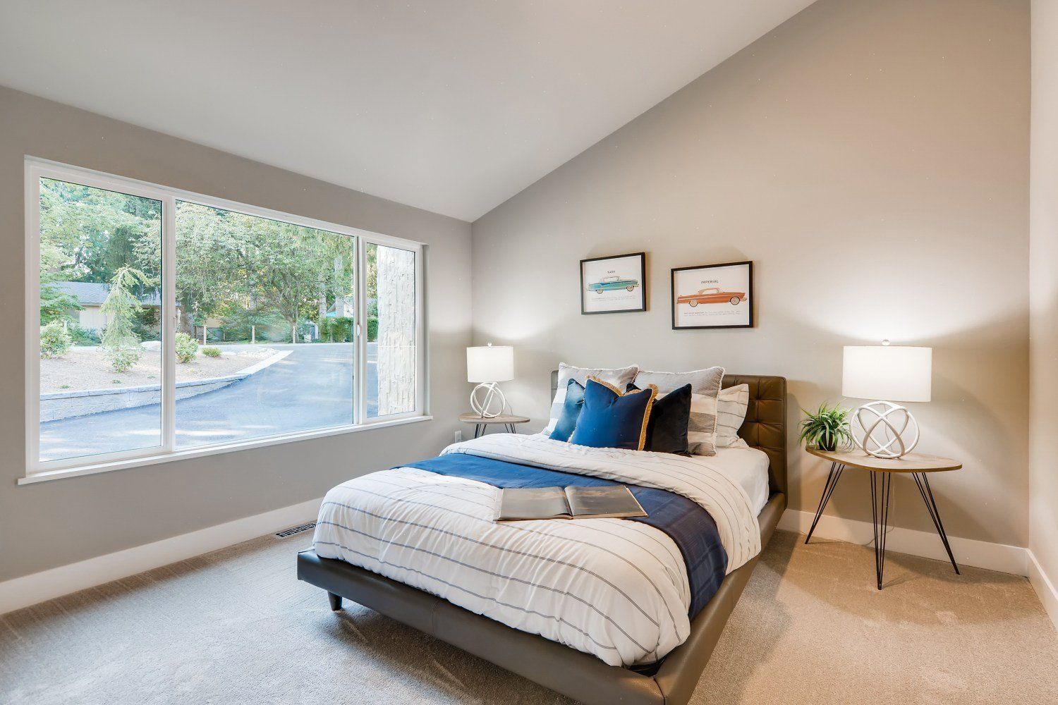 Bedroom with bed, large window, neutral walls, and a side table.