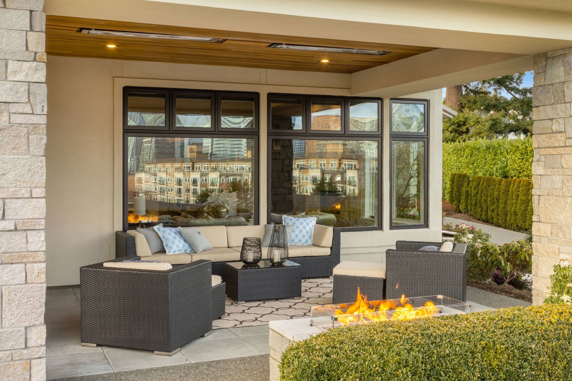 Outdoor patio with wicker furniture, fire pit, and large windows, view of city reflection.