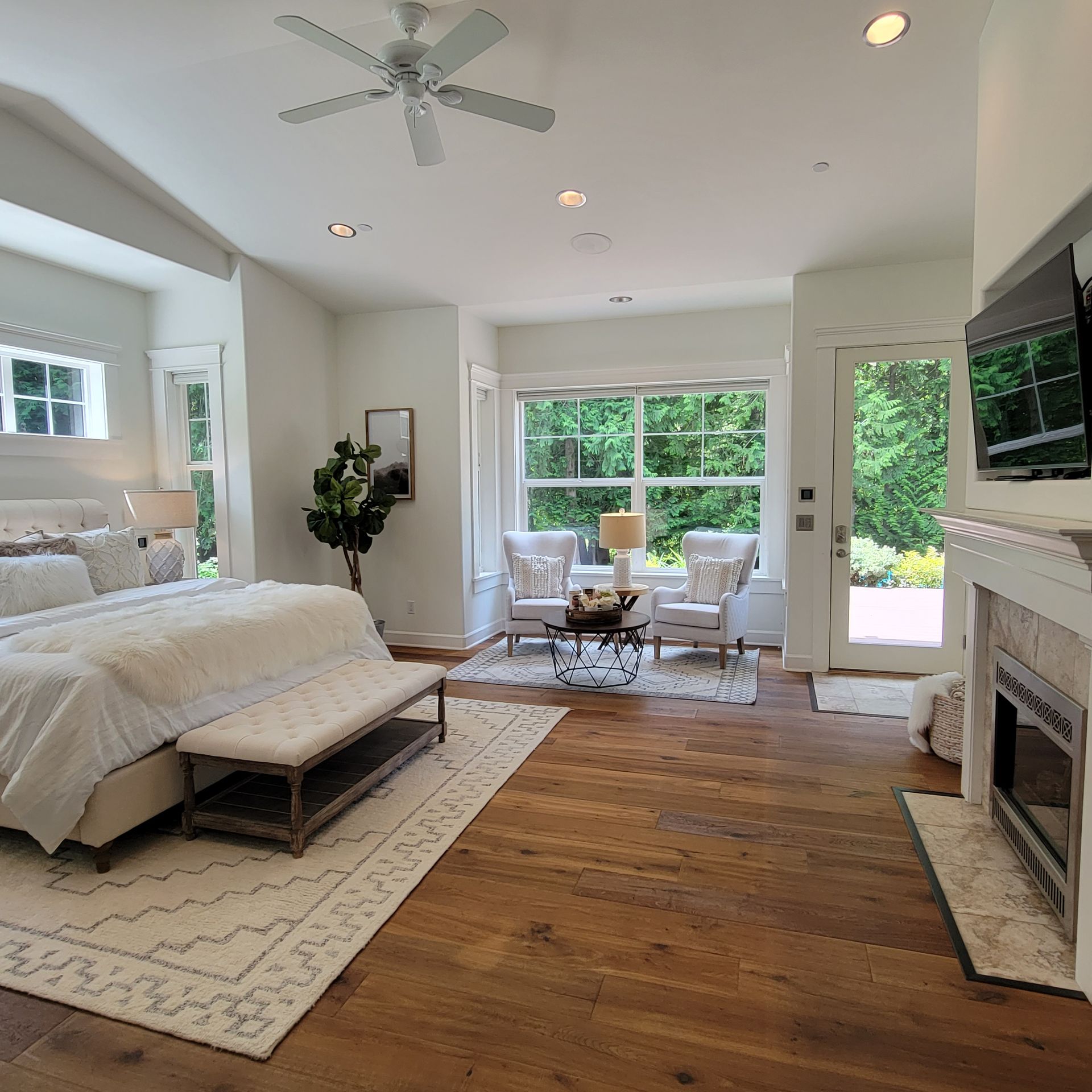 Bedroom with a bed, fireplace, seating area, windows, and a door to the outside.
