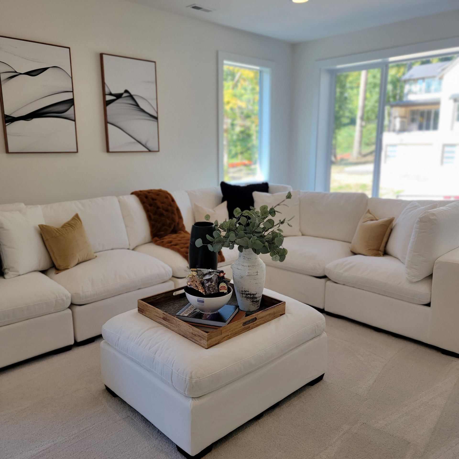 White sectional sofa in a bright living room, with a tray on the ottoman and art on the wall.