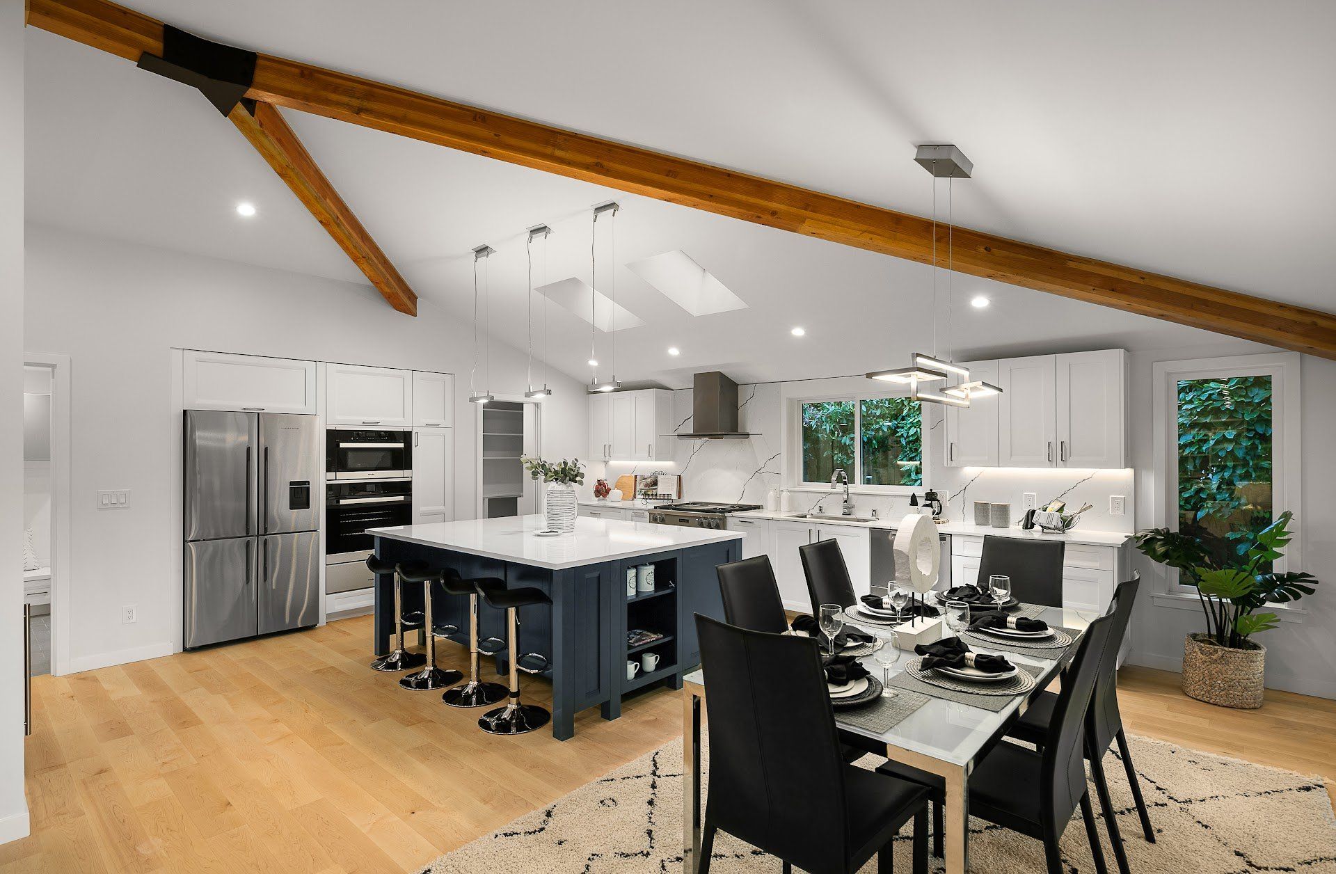 Modern kitchen and dining area with white cabinets, navy island, wooden beams, and a formal dining table.