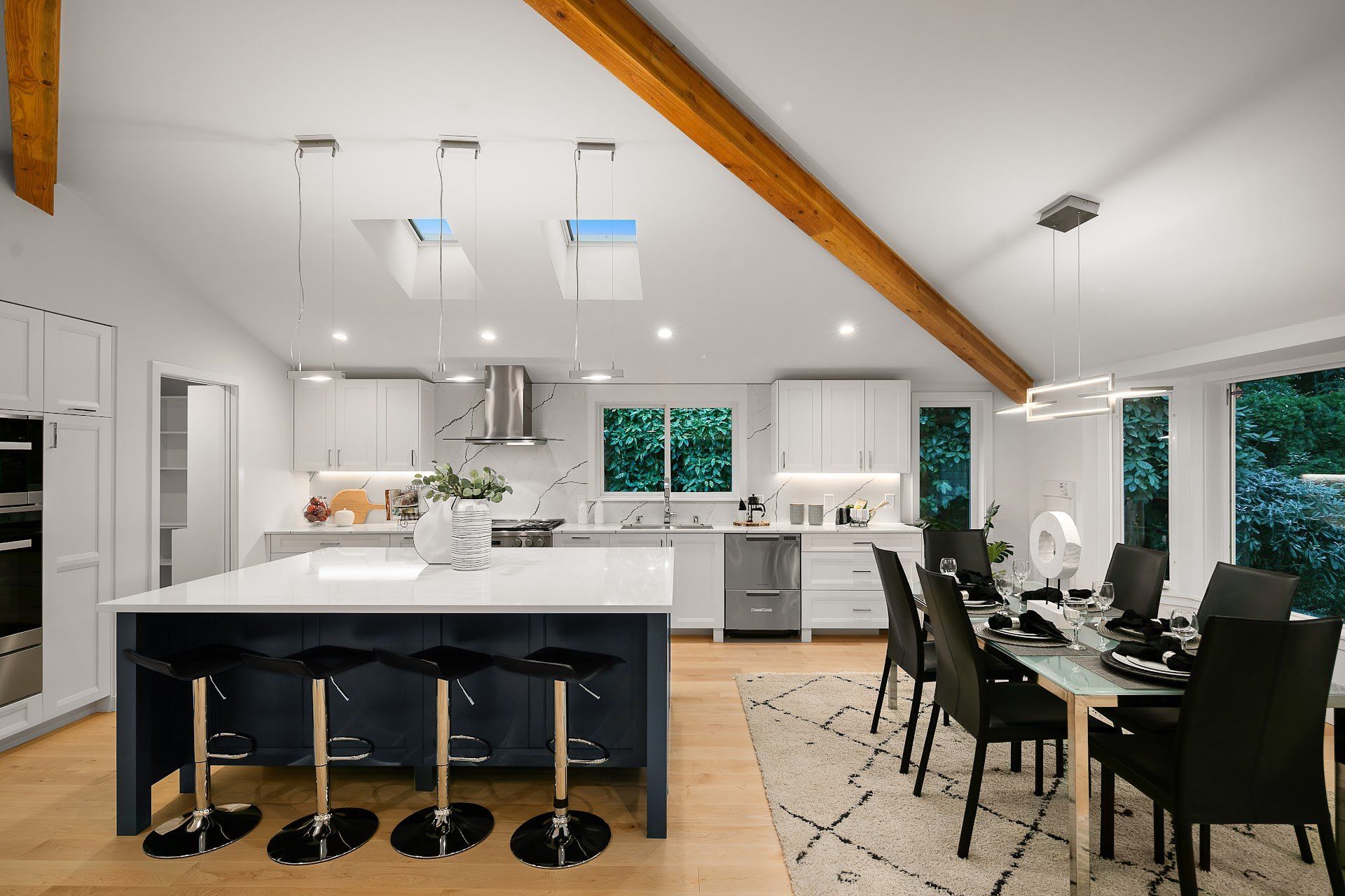Modern kitchen and dining room with island, seating, white cabinets, and dark seating around a dining table.