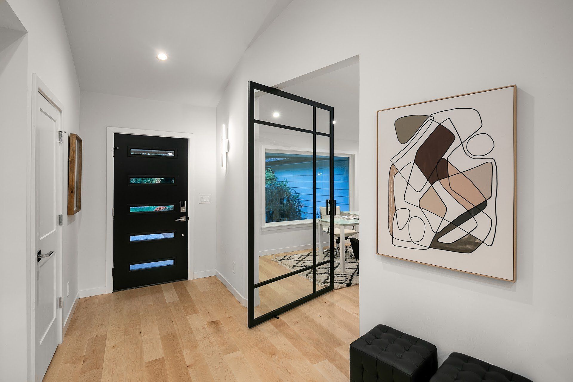 Hallway with a black door, art, and a metal and glass door leading to a room with a window.